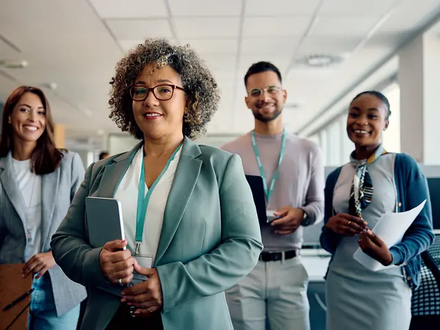 A woman holding a tablet stands with her team in a bright office.
